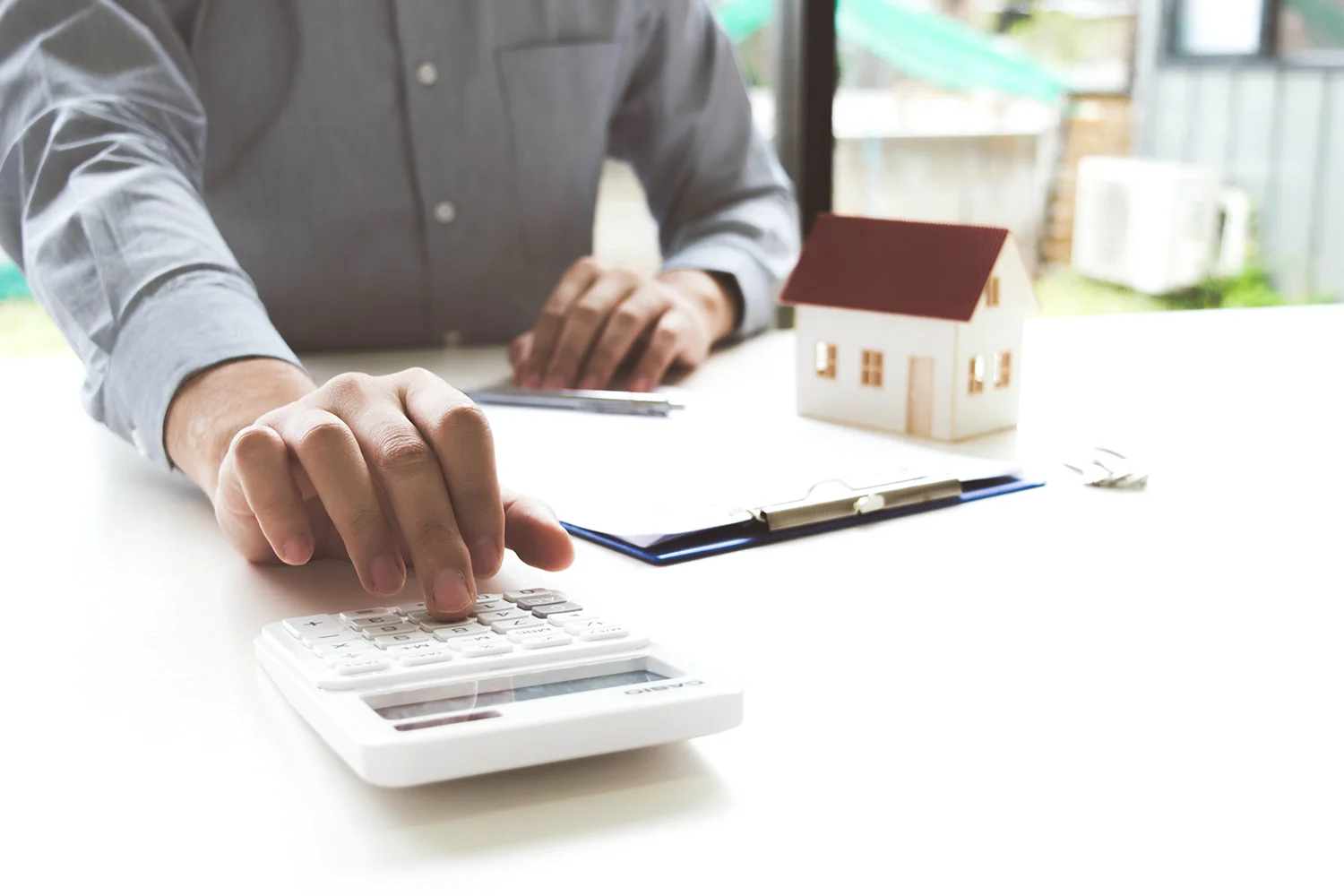 Homeowner calculating property taxes with a calculator and house model for Johnson County property tax protest preparation. 
