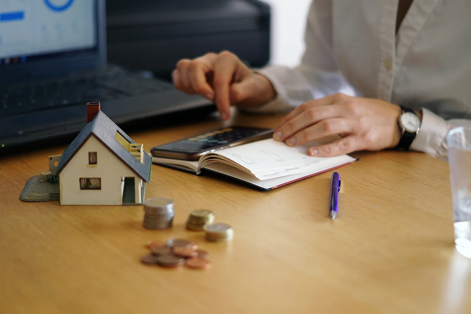 Property tax calculation with home model, coins, and notebook on desk, representing professional property tax protest services by Tax Cutter.
