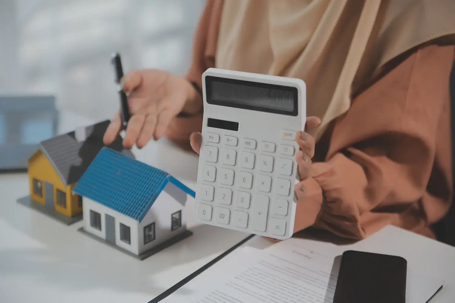 Homeowner holding calculator beside house models and property tax documents, representing Texas property tax protest services by Tax Cutter.