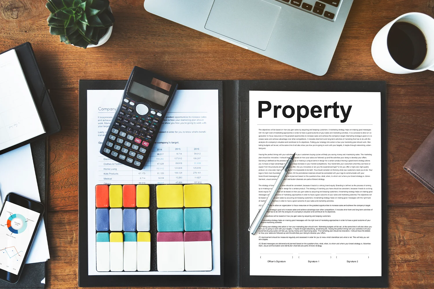 Property tax documents and financial analysis materials on a desk, including a calculator, property report, laptop, and charts used for reviewing property values. 