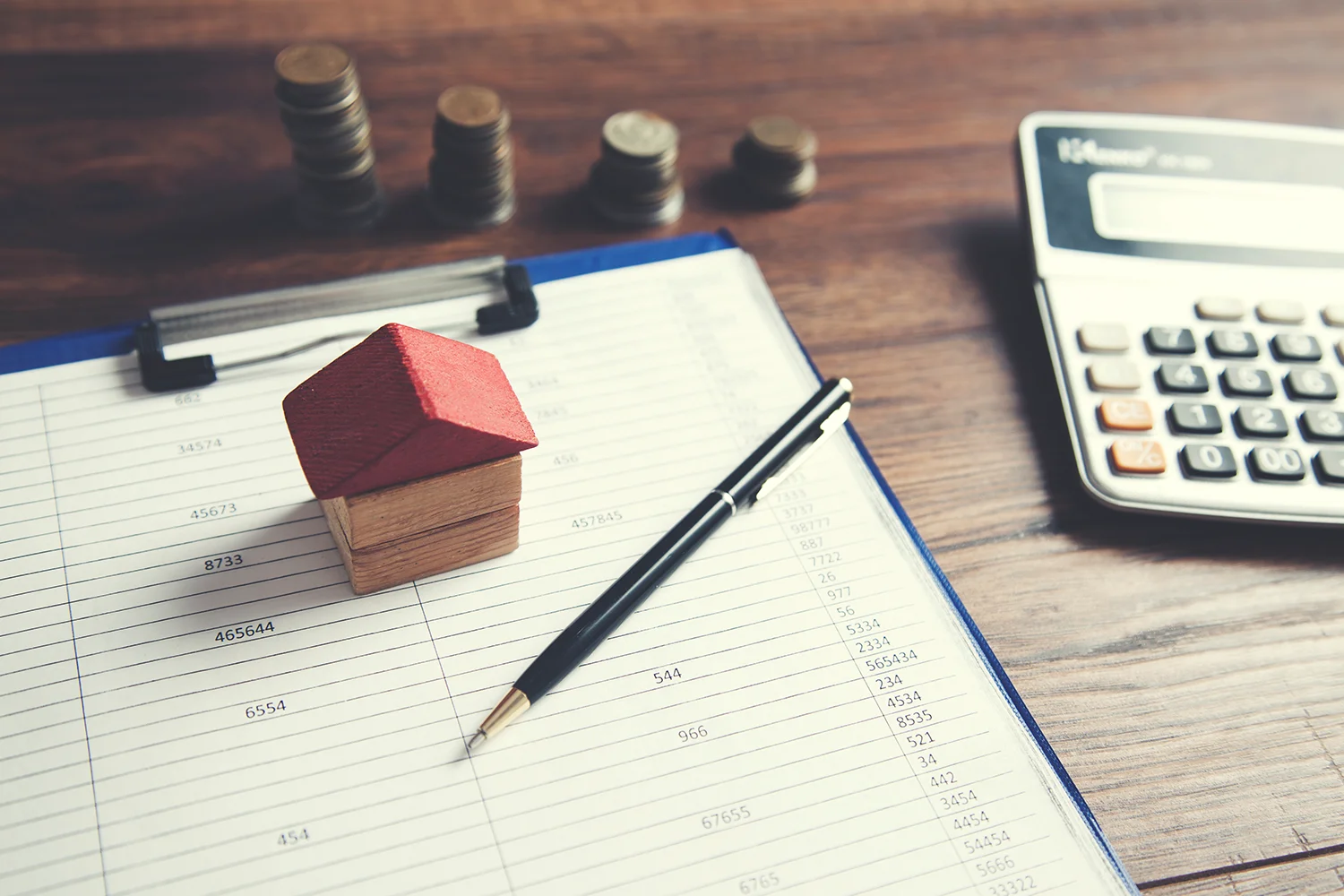 Property tax calculation with house model, ledger, coins, and calculator, representing Houston property tax protest services by Tax Cutter.