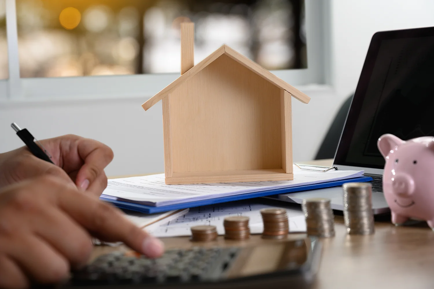 Person calculating property taxes with a calculator, a wooden house model, and coins, symbolizing Tax Cutter's services in helping homeowners reduce property taxes in Houston