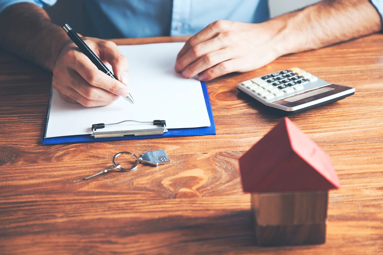 Person reviewing property tax documents and using a calculator, with a small house model and keys, symbolizing the property tax protest services of Tax Cutter.