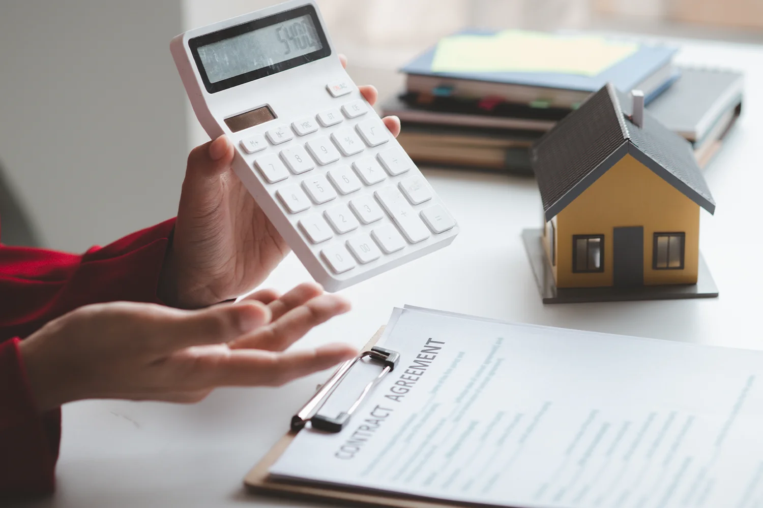 Homeowner calculating property tax costs with calculator and house model, reviewing documents for property tax protest.