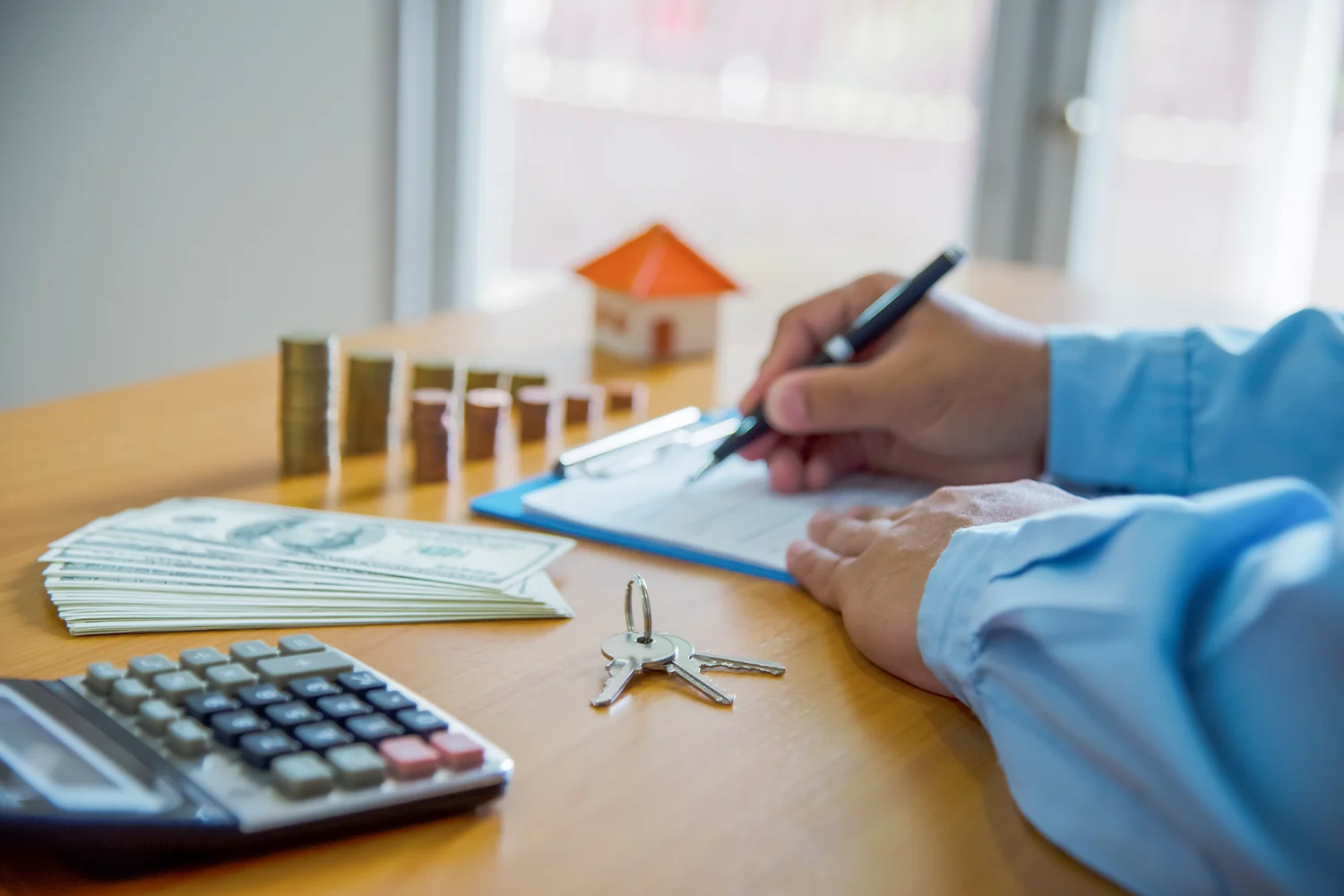 Person signing property tax appeal paperwork with money, coins, keys, and a calculator, symbolizing savings and tax reduction services from Tax Cutter. 