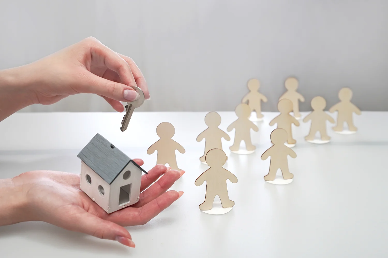 Hand holding a key over a house model, with wooden figures representing homeowners, symbolizing Tax Cutter's property tax services for helping people save money.