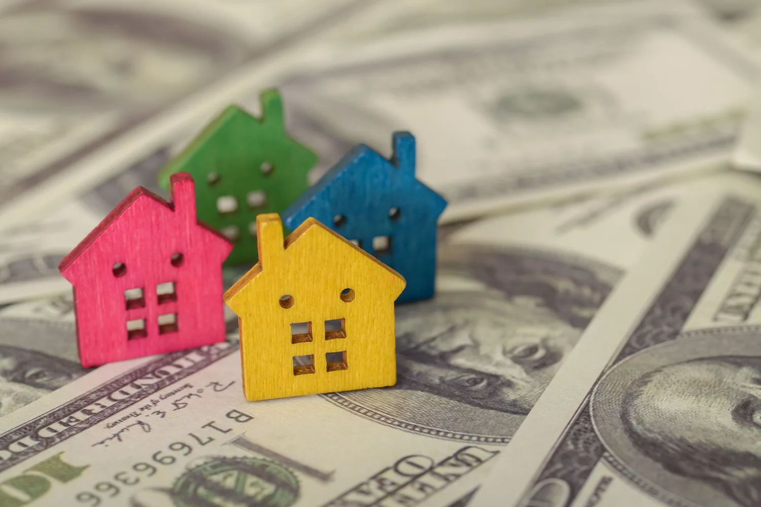 Colorful house models on U.S. dollar bills representing Houston property tax assessments and potential tax savings.