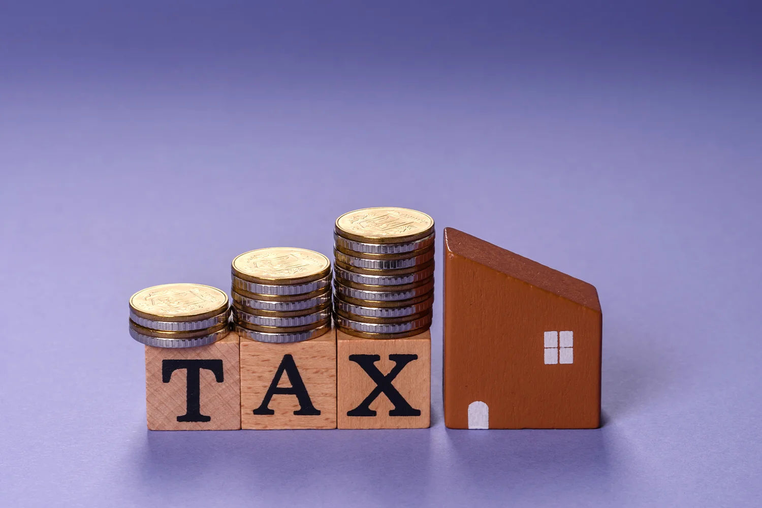 Property tax concept with coins stacked on TAX blocks next to house model, representing Houston property tax protest savings by Tax Cutter 