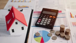 Small model house with a red roof placed on financial documents alongside a calculator, coins, and charts, representing property taxes, budgeting, and home expenses.