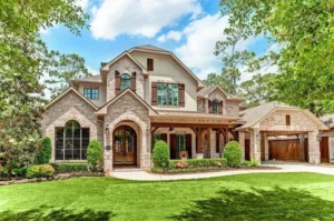 Large two-story brick home with arched windows, a covered front porch, wooden garage doors, and a landscaped lawn surrounded by trees.