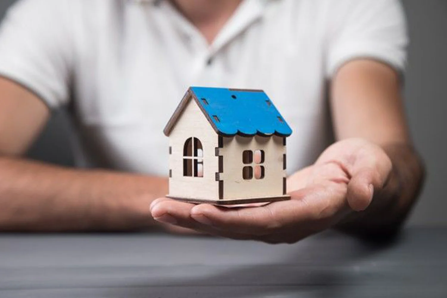 Person holding a small wooden model house in their hand, representing homeownership and property tax protest services by Tax Cutter in Houston.