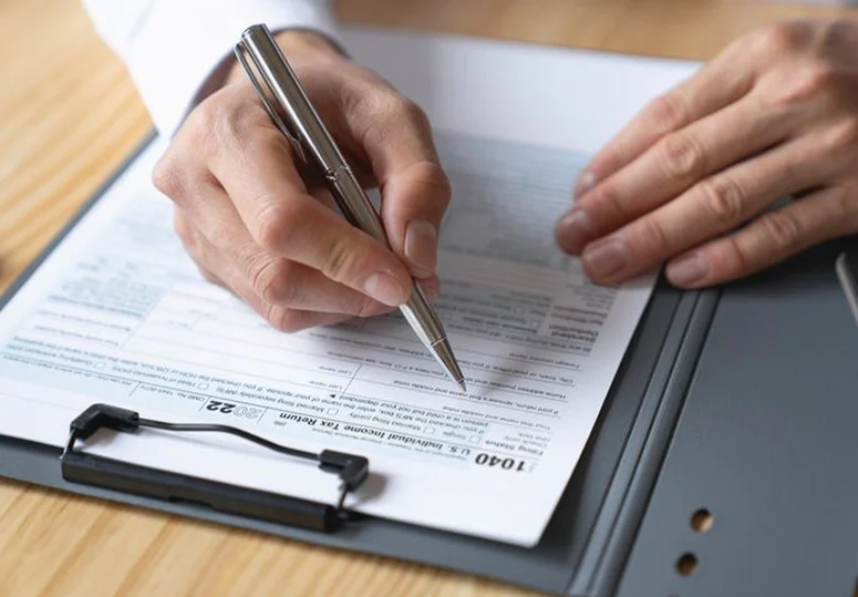 Close-up of person signing a tax form on a clipboard, representing property tax filing, documentation, and appeal preparation.