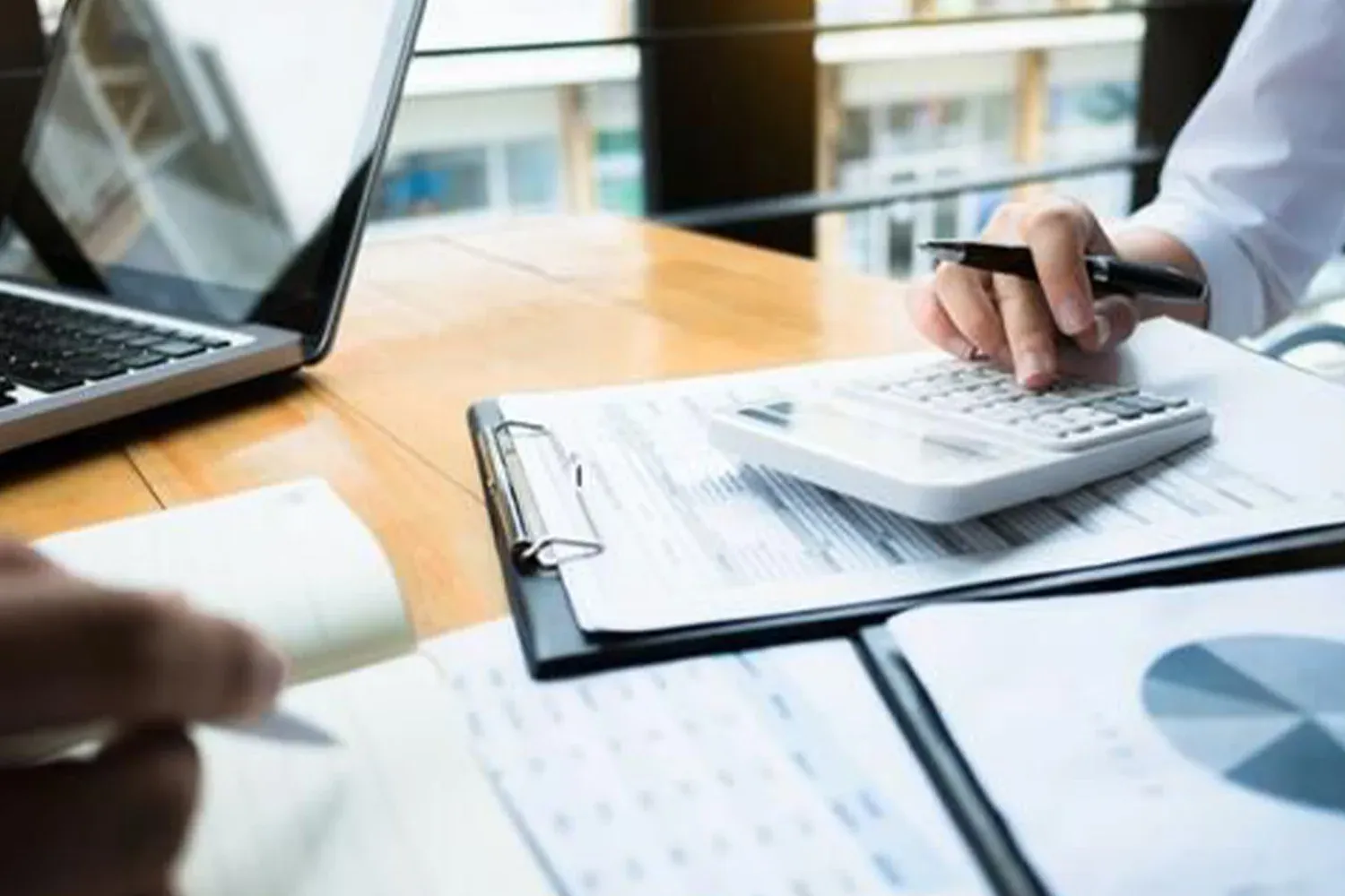 Person using calculator with financial reports and charts on desk, representing tax calculations, property assessment, and financial analysis.