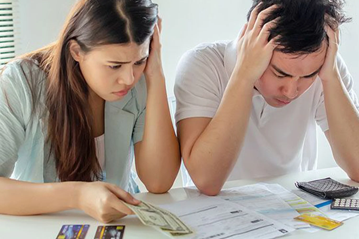 A stressed couple reviewing bills and finances at a table, holding cash and looking worried about expenses and budgeting.