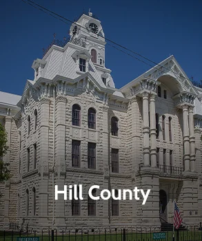 Hill County Courthouse in Texas featuring ornate limestone architecture, arched windows, and a historic clock tower under a clear blue sky.