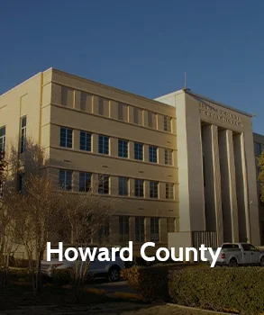 Howard County Courthouse in Texas with modern beige facade, vertical columns, and parked cars in front under a clear blue sky.