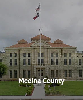 Medina County Courthouse in Texas with light stone exterior, symmetrical design, central walkway, and landscaped grounds under a cloudy sky.