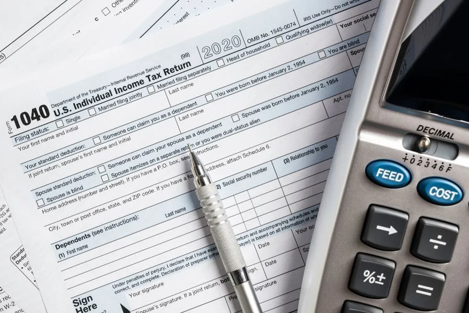 IRS Form 1040 with pen and calculator, representing income tax filing, financial calculations, and tax preparation documents.