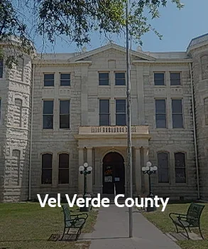 Val Verde County Courthouse in Texas with stone exterior, arched entrance, and symmetrical design surrounded by lawn and benches.