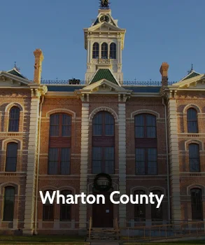 Wharton County Courthouse in Texas with red brick facade, tall central clock tower, and symmetrical historic architecture.